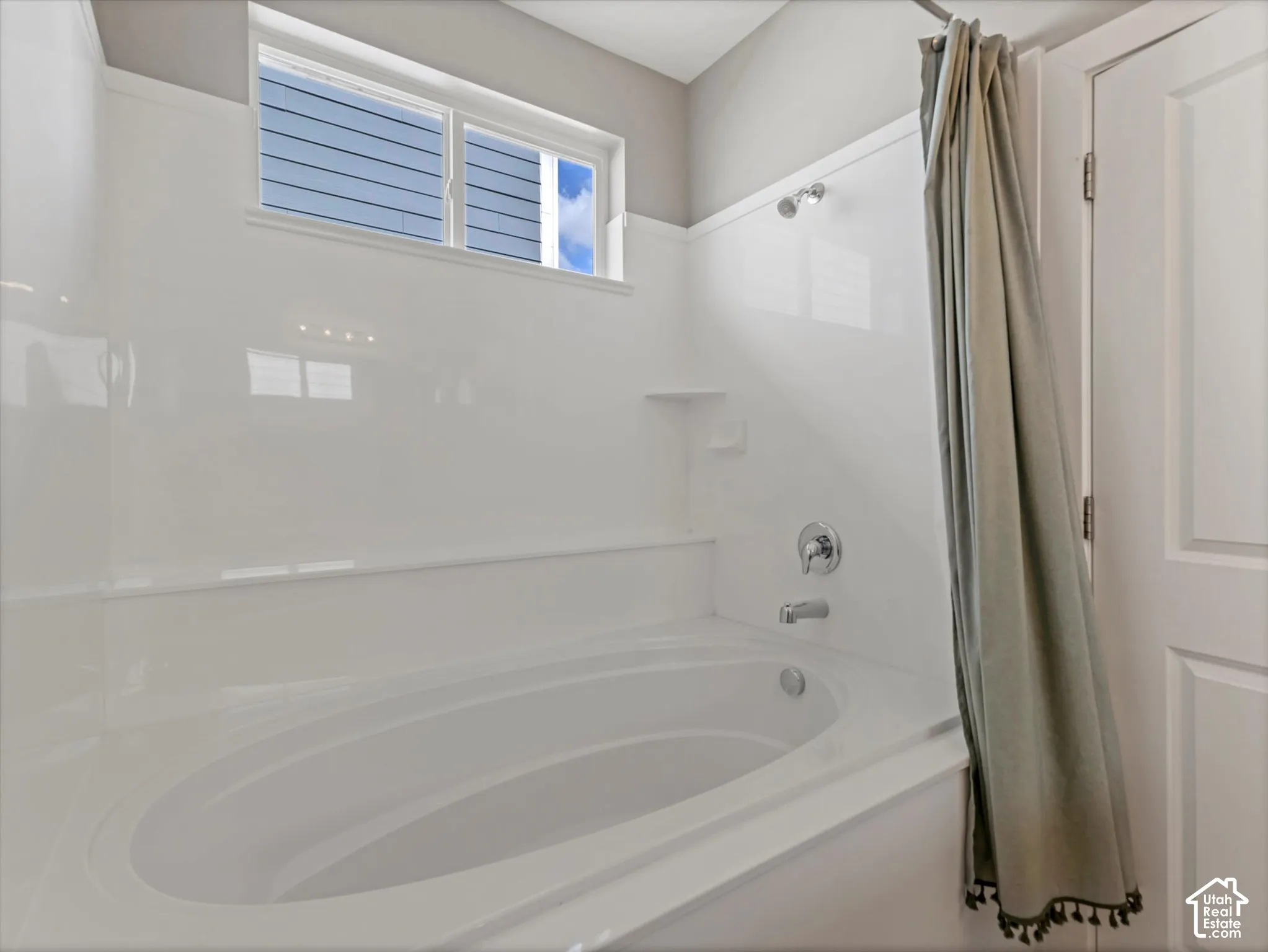 Built-in soaking tub with chrome fixtures, integrated shelving, and a privacy window with horizontal blinds