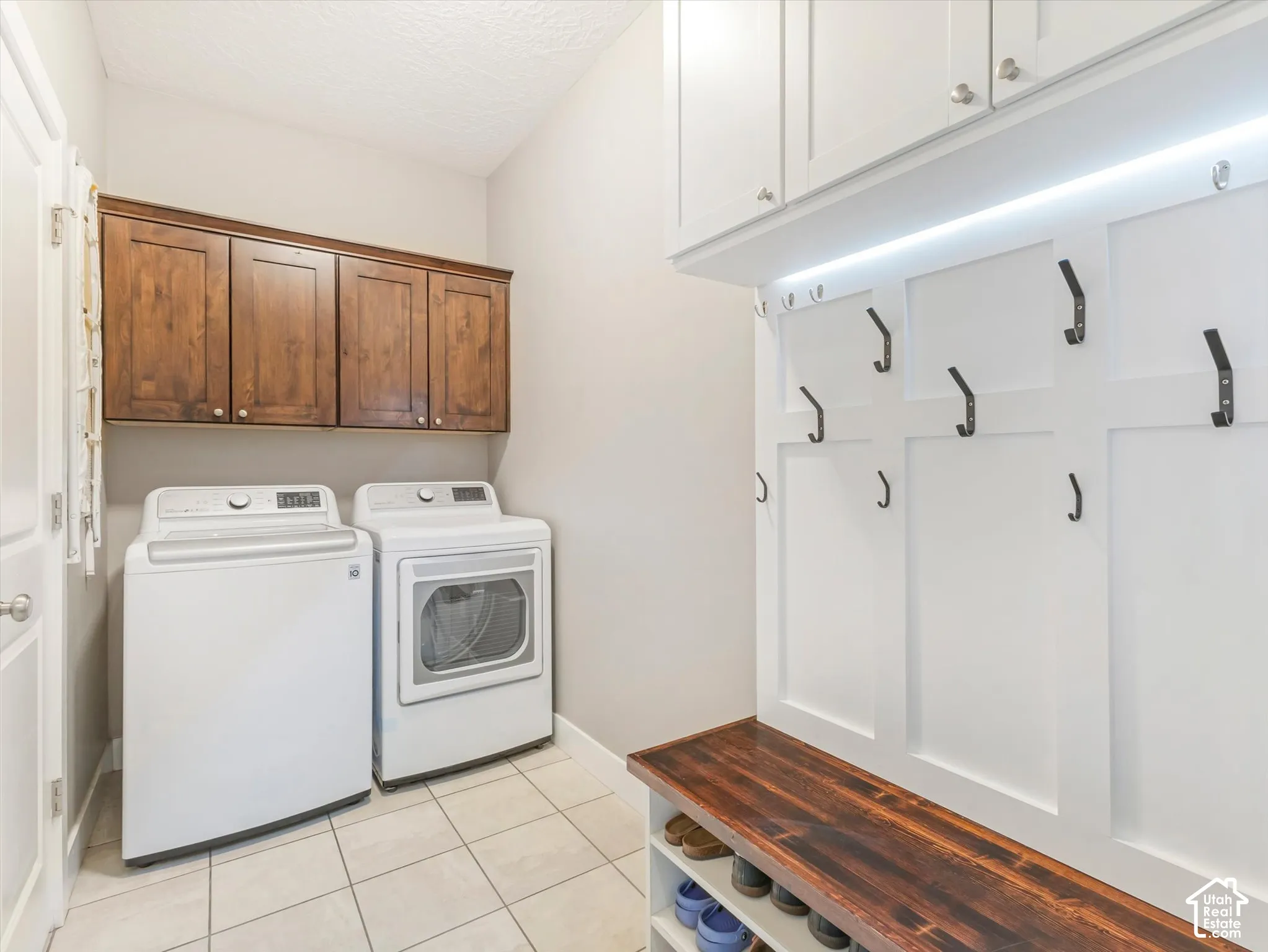 Laundry area featuring tile flooring, dark wood-finish cabinetry, and white built-in storage with a wood-finish bench and coat hooks