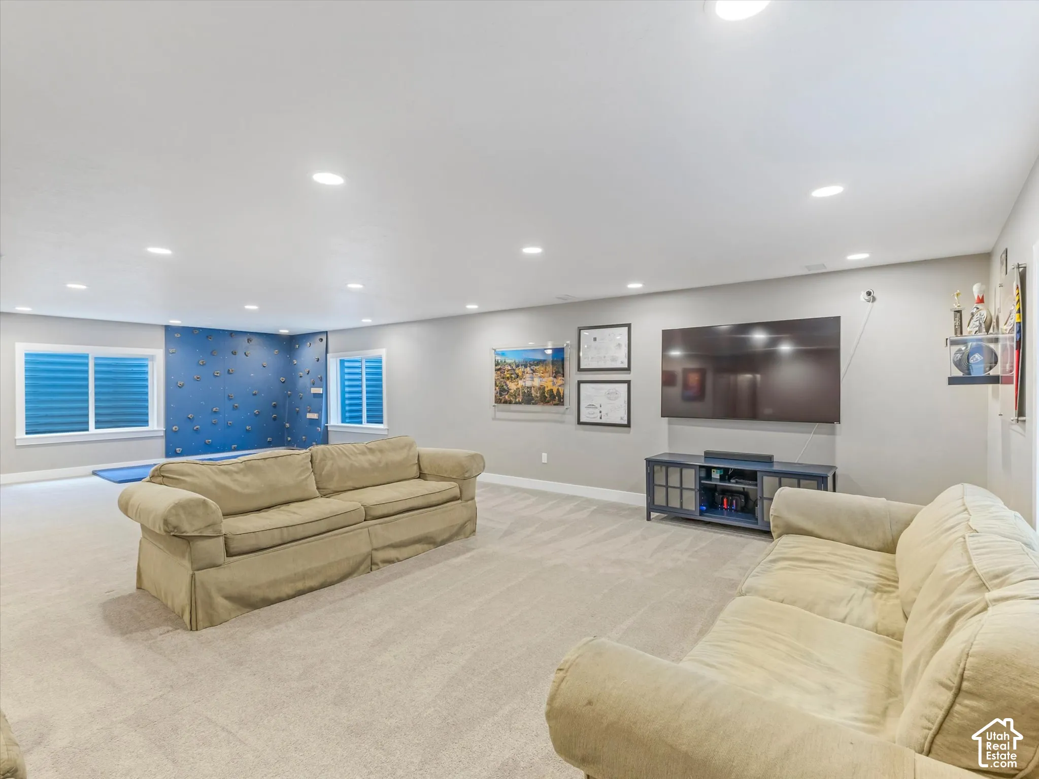 Recessed ceiling lighting, light gray wall paint, light-colored carpet flooring, two windows with horizontal blinds, and a blue accent wall