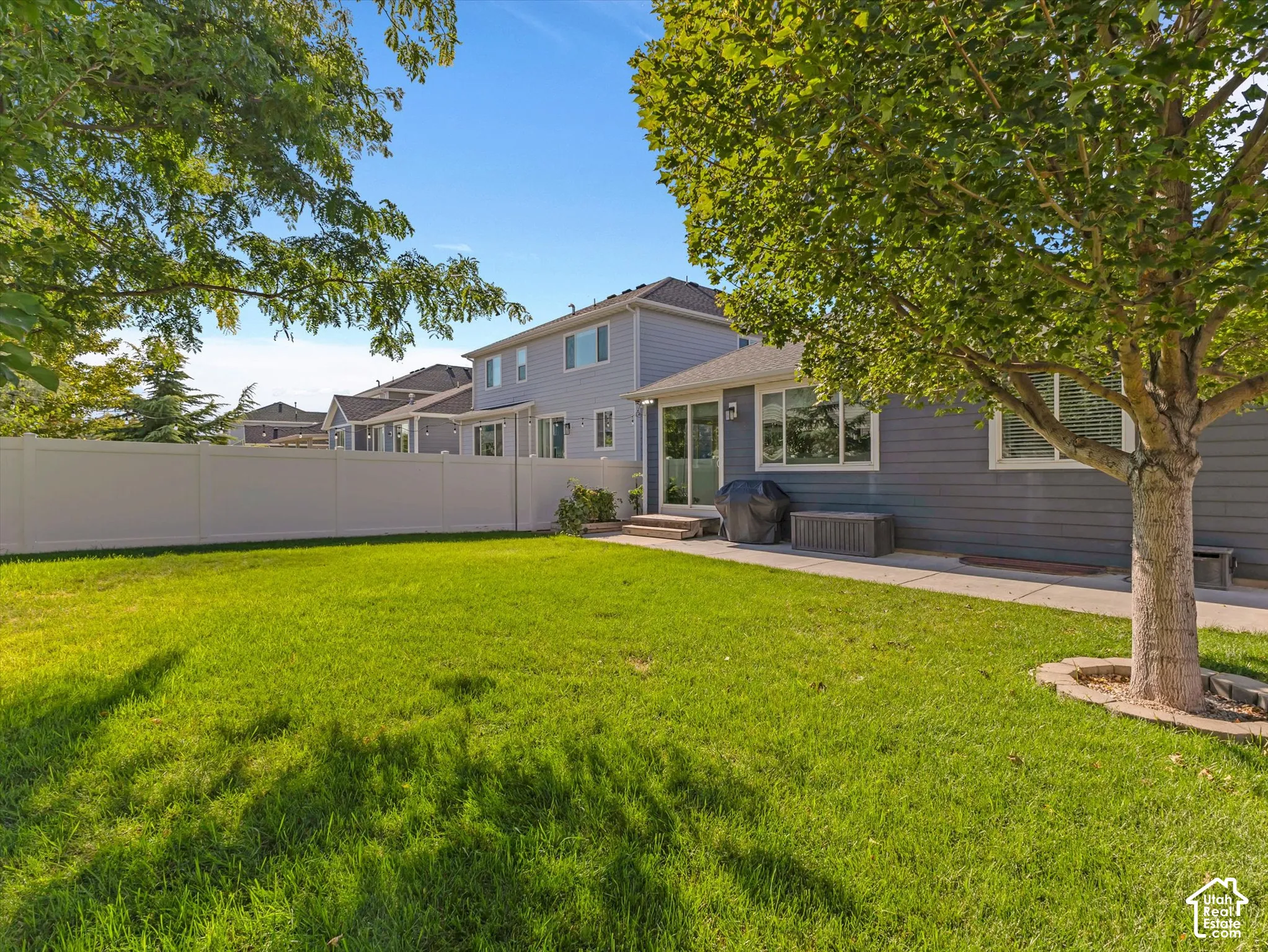 Spacious green yard with privacy fencing, mature trees, and a concrete patio