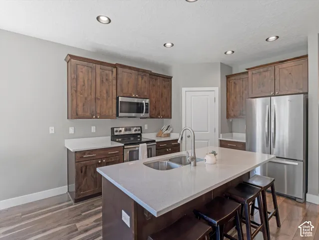 Kitchen featuring recessed lighting, wood-finish flooring, stainless steel appliances, dark wood cabinetry, and light-toned countertops