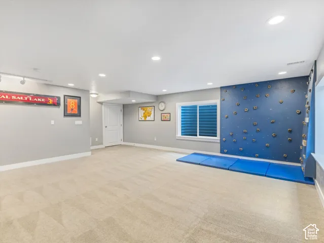 Spacious room featuring neutral carpet, recessed lighting, a built-in climbing wall, a window with horizontal blinds, and a solid core interior door