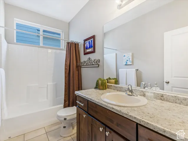 White tile flooring, wood-finish vanity with an integrated sink, granite-look countertop, and a built-in bathtub with subway tile surround