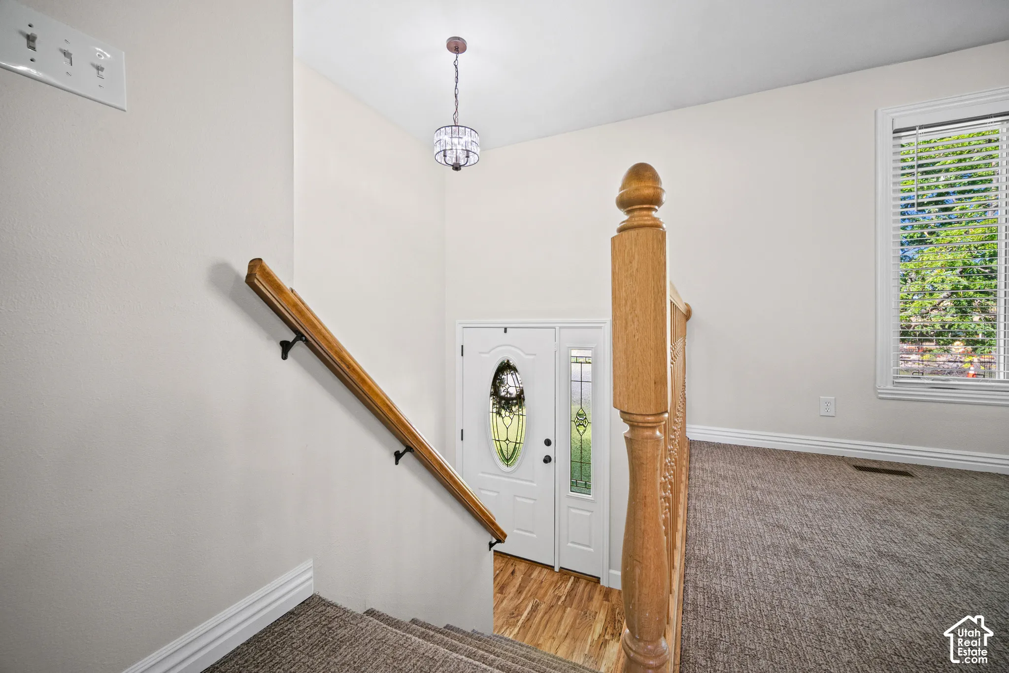 Elegant staircase landing featuring a natural wood handrail with decorative newel post, warm wood-finish flooring, and soft pendant lighting