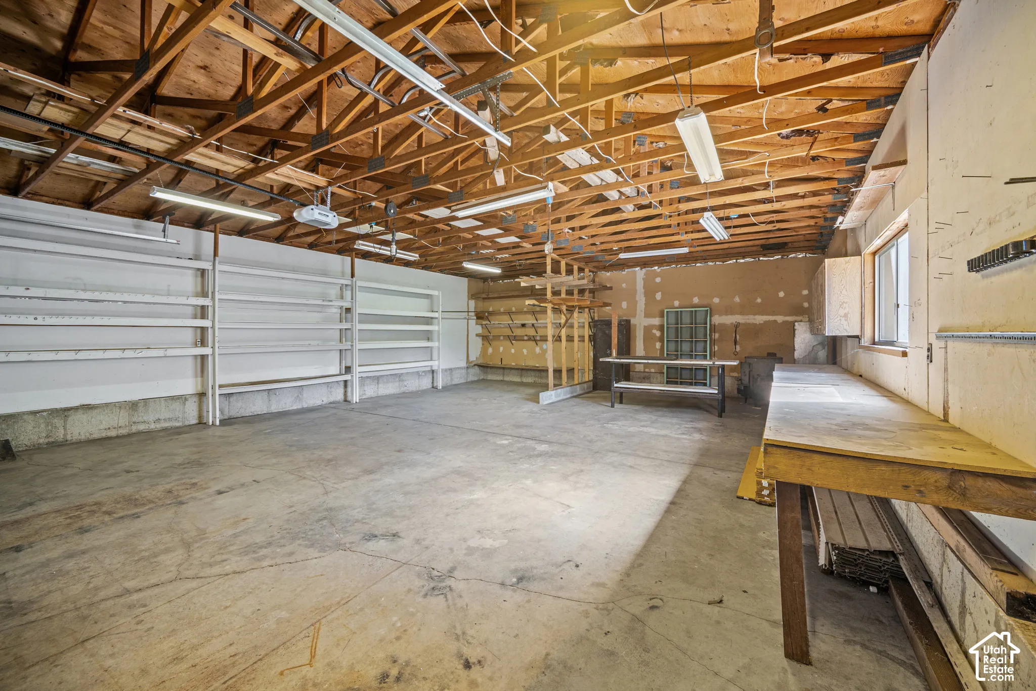 Concrete flooring, exposed wood beam ceiling, built-in shelving, workbenches, and window