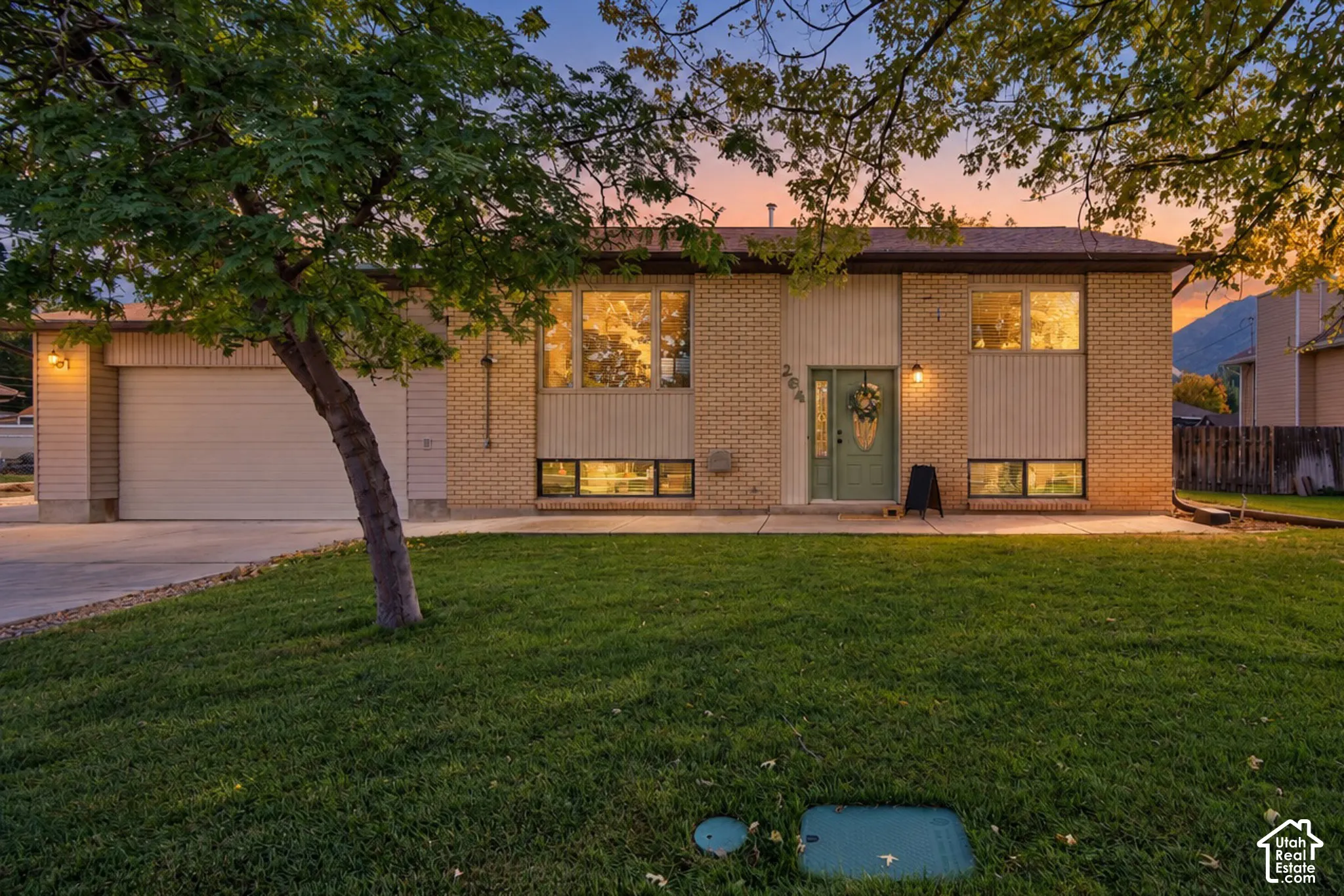 Brick and vertical siding exterior with an attached garage, mature front tree, and concrete driveway