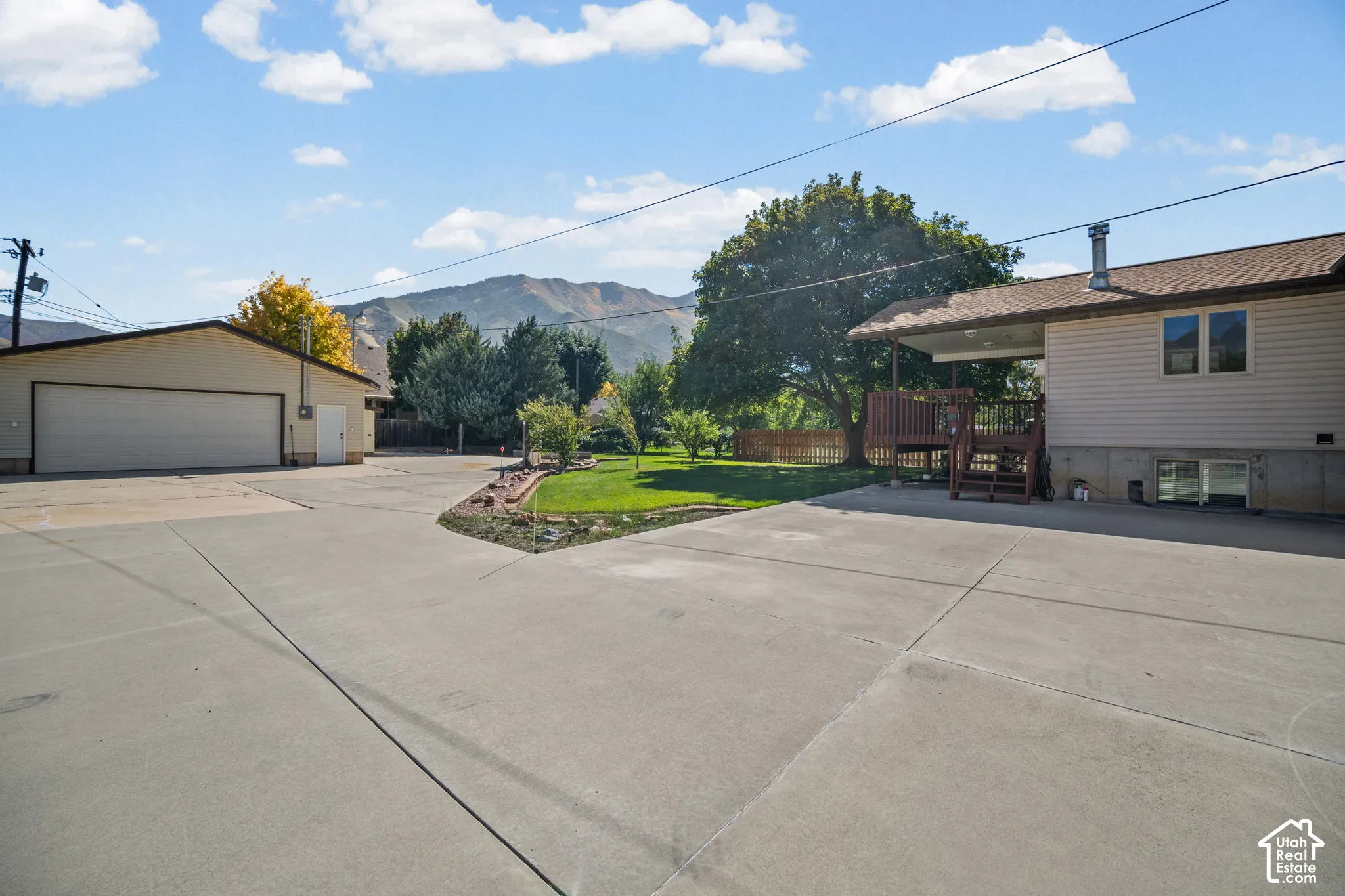Expansive concrete driveway, detached garage with dual bay door, and a multi-level wood deck