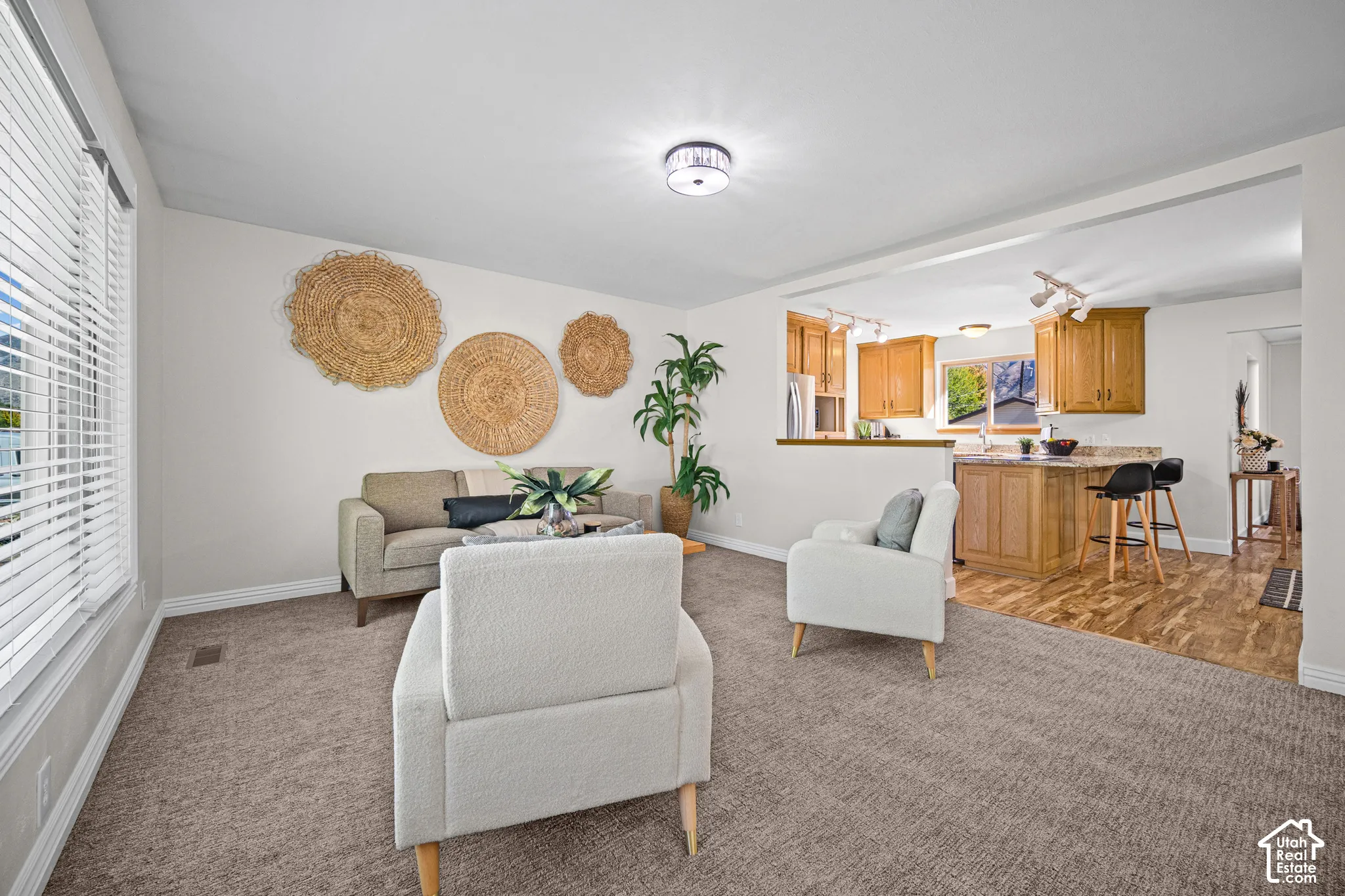 Open-concept living area featuring neutral-toned upholstered seating, woven wall accents, and abundant natural light from large windows