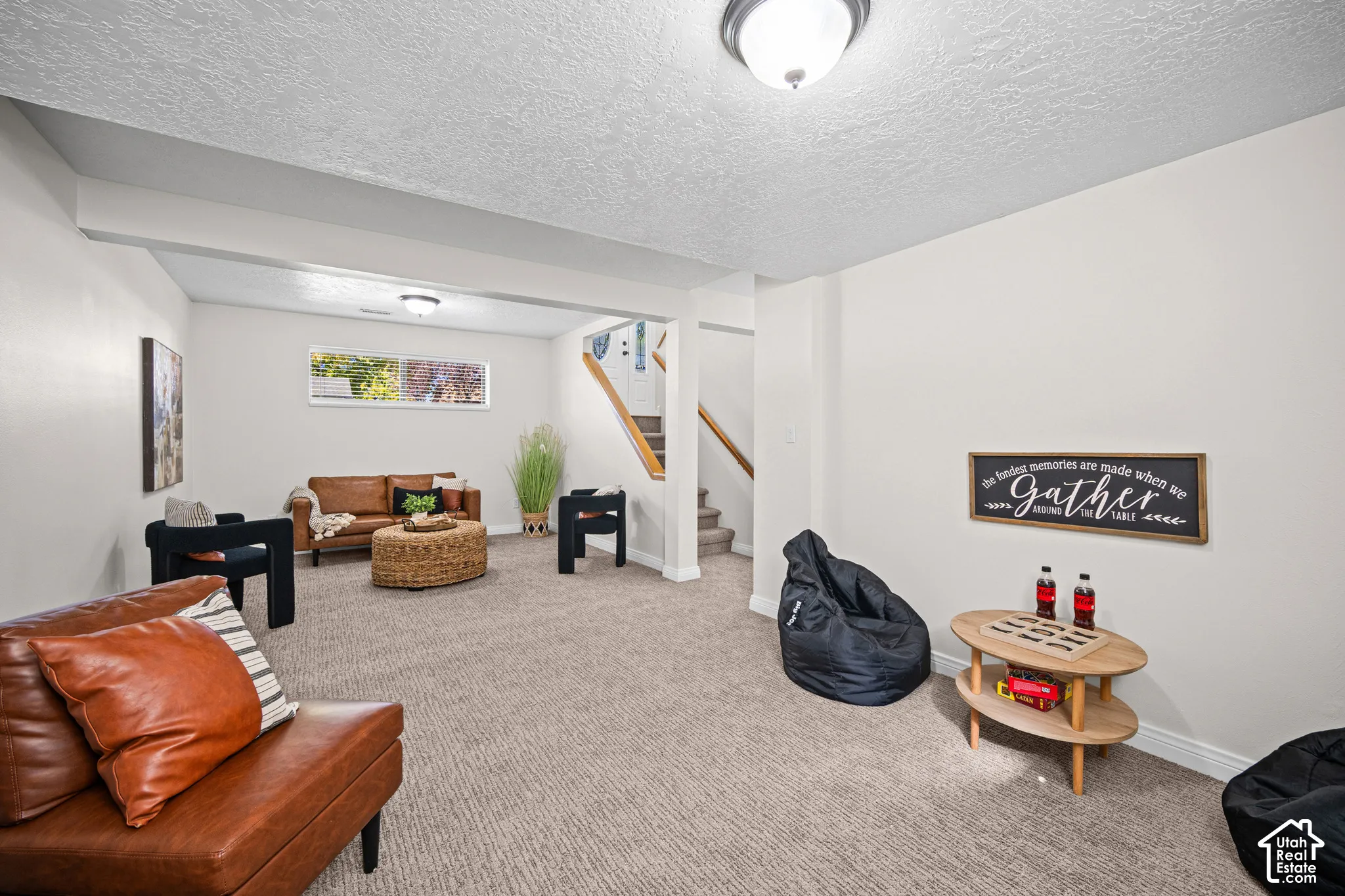 Carpeted recreation room with white painted walls, a horizontal window, and a visible staircase with wood railing