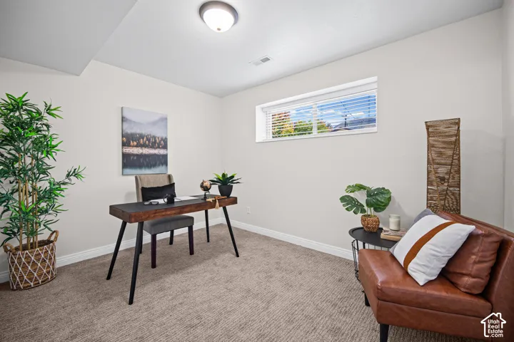 Dedicated home office featuring a mid-century modern wood desk with tapered legs, neutral carpeting, and abundant natural light from a transom window