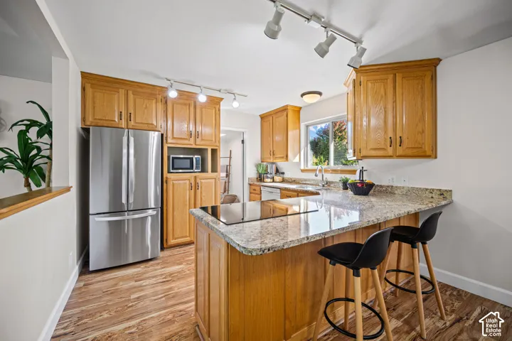 Kitchen featuring wood cabinetry, stainless steel appliances, granite countertops, an integrated cooktop, and wood-finish flooring