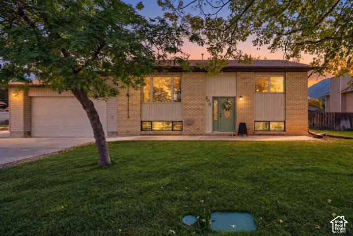 Brick and vertical siding exterior with an attached garage, mature front tree, and concrete driveway