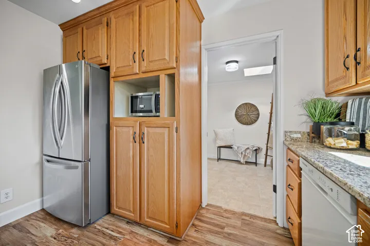 Modern kitchen featuring stainless steel French-door refrigerator, wood-finish cabinetry with ample storage, granite-style countertops, built-in microwave, and wood-finish flooring throughout
