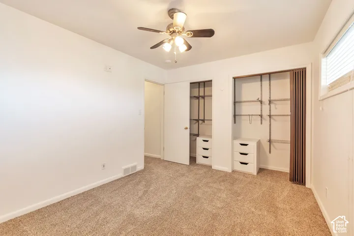 Carpeted room featuring a ceiling fan with light fixture, window with blinds, and two closets with built-in shelving and drawer units