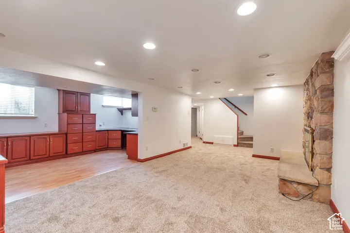 Recessed lighting, built-in cabinetry, wood-finish flooring, stone-clad fireplace with hearth, and staircase with wood railing