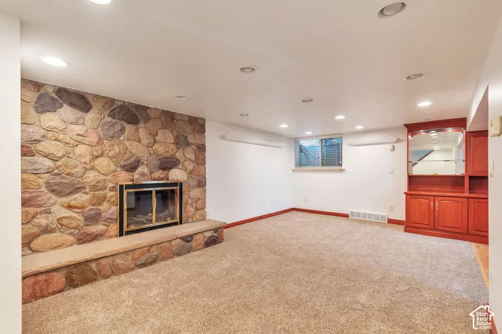 Stone-clad fireplace with hearth, recessed lighting, built-in cabinetry, and neutral carpet flooring
