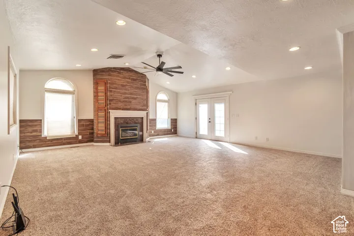 Vaulted ceilings with recessed lighting, integrated ceiling fan, stone-finish fireplace with mantel, arched windows, and French doors