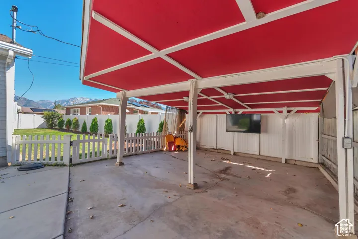 Covered carport with concrete flooring, white picket fencing, and an adjacent fenced lawn area