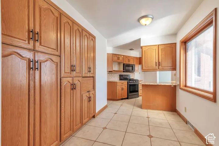 Extensive wood cabinetry, patterned tile flooring, wood-framed window, black kitchen appliances, and a breakfast bar with a stone countertop