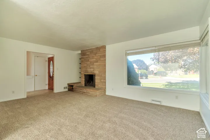 Living area with carpet flooring, a stone-clad fireplace, and a large picture window