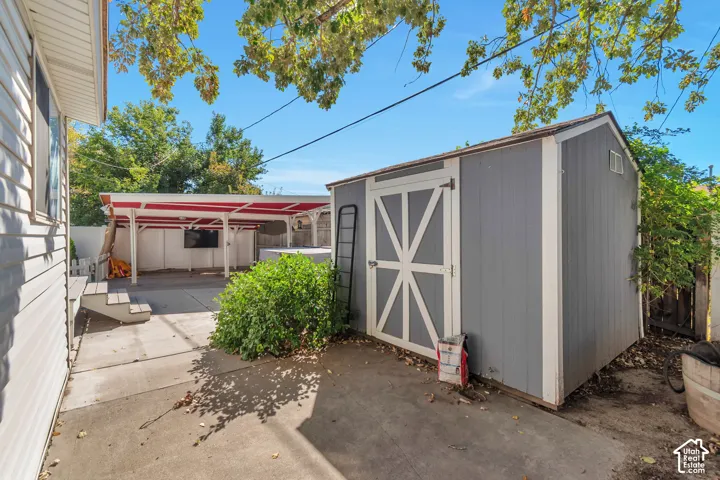 Detached storage shed with white trim, covered patio area, and concrete slab