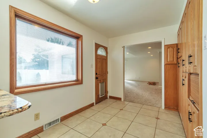 Tile flooring, wood-finish cabinetry, built-in storage, wood-frame window, and a wood-panel door
