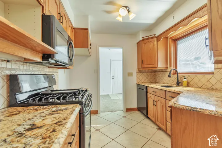 Kitchen featuring wood cabinetry, stone-finish countertops, stainless steel appliances, and tile flooring