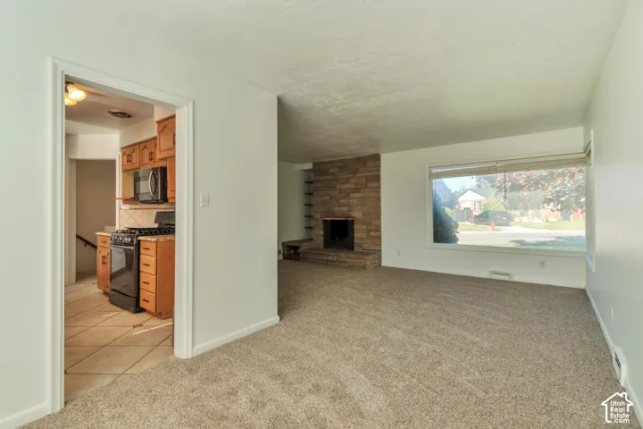 Living space with neutral carpeting, a large front-facing window, and a stone-clad fireplace