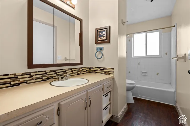 Bathroom featuring wood-finish flooring, a single vanity with an integrated sink, a multi-paneled medicine cabinet, a tiled backsplash, and a tub with a window