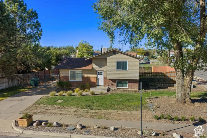 Split-level residence featuring a brick foundation and siding exterior, a front yard with mature trees, and a driveway