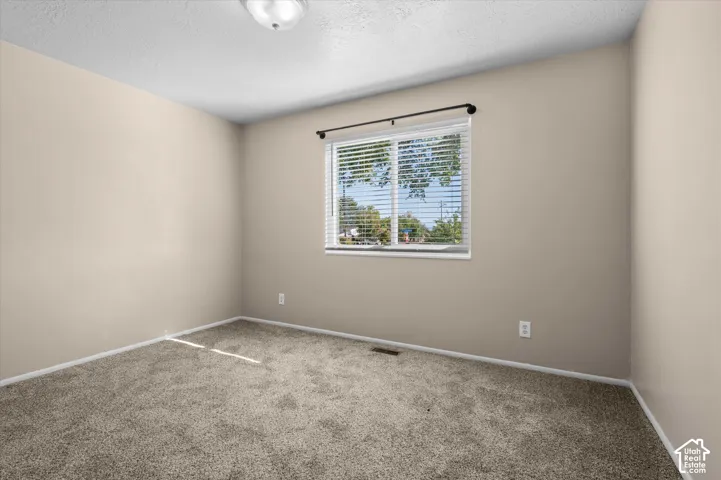 Bright secondary bedroom featuring neutral wall finishes, carpet flooring, and a large double-hung window with natural light and exterior views