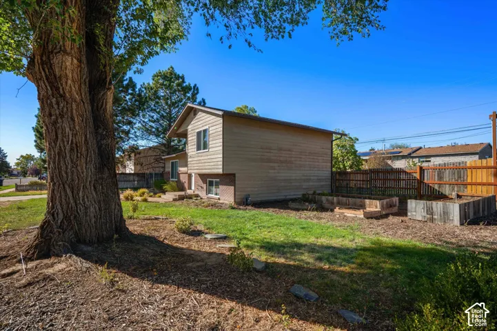 Split-level residence featuring a wood fence, raised garden beds, and mature trees