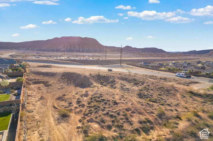 Expansive undeveloped land featuring a paved road, mountain backdrop, and surrounding residential properties