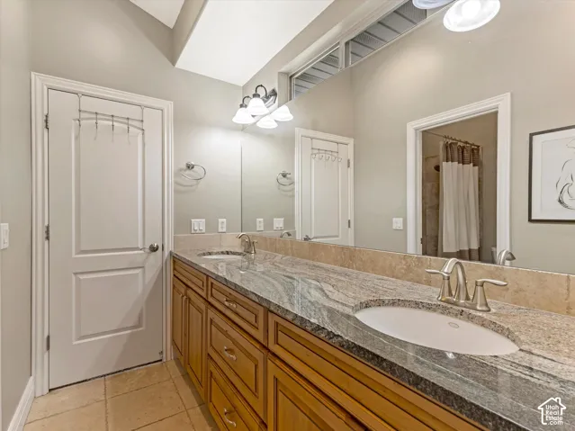 Dual vanity with wood-finish cabinetry, stone countertop, undermount sinks, and tile flooring