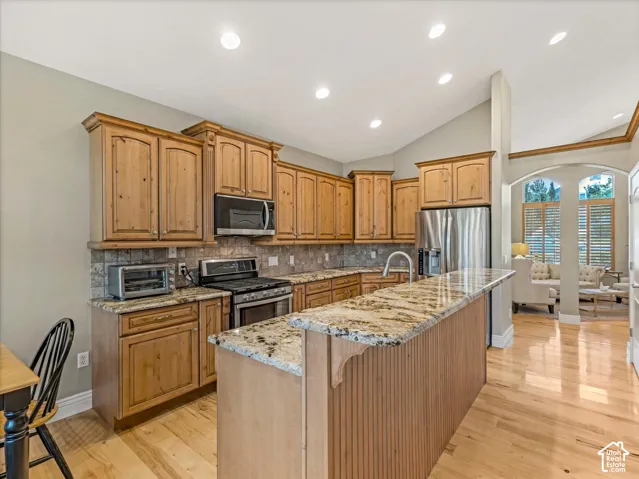 Kitchen featuring wood cabinetry, granite countertops, tile backsplash, stainless steel appliances, and wood-finish flooring