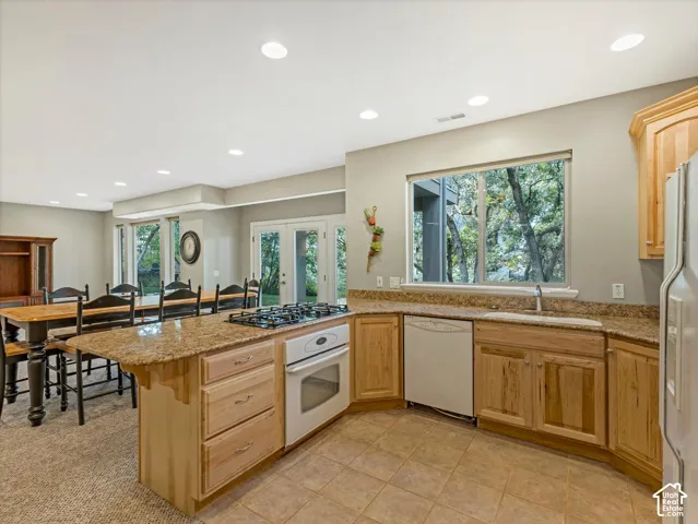 Kitchen featuring an integrated cooktop and oven, tile flooring, wood cabinetry, stone countertops, and a full-size window