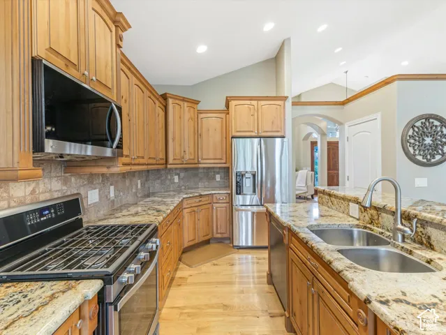 Wood-finish cabinetry, stainless steel appliances, stone countertops, integrated double basin sink, and tile backsplash