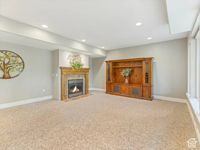 Recessed lighting, light-toned carpeting, a built-in fireplace with a stone surround, wood mantel, and hearth, and a large built-in wood entertainment center