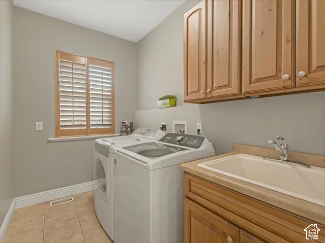Tiled flooring, wood-finish cabinetry, built-in utility sink, and window with plantation shutters
