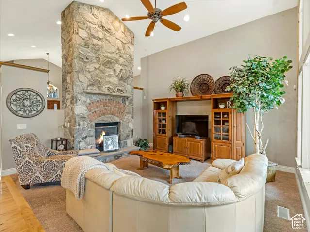 Stone fireplace with a brick arch and hearth, vaulted ceiling with recessed lighting, wood-finish ceiling fan, and carpeted flooring