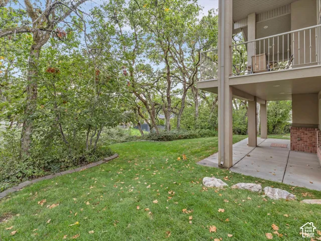 Expansive grassy lawn with mature trees, a concrete patio, and an upper-level balcony with metal railing