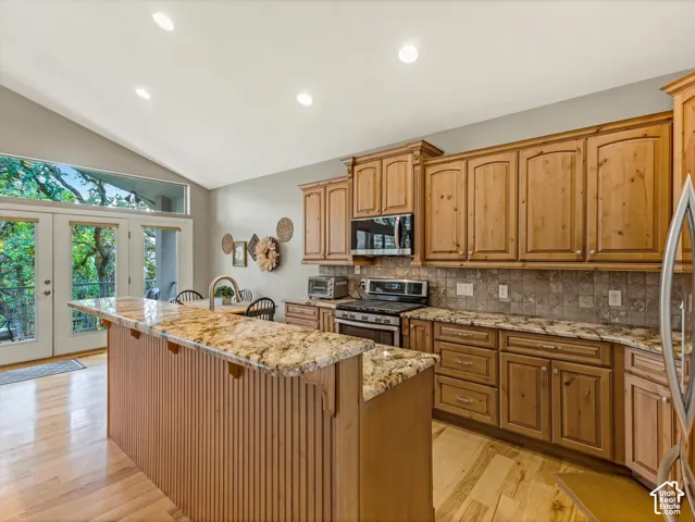 Vaulted ceilings with recessed lighting, wood-finish flooring, wood cabinetry, granite countertops, and a tile backsplash