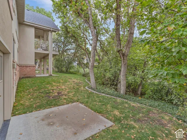 Expansive green space featuring a concrete patio, mature trees, and a ground-level covered patio with a second-story balcony