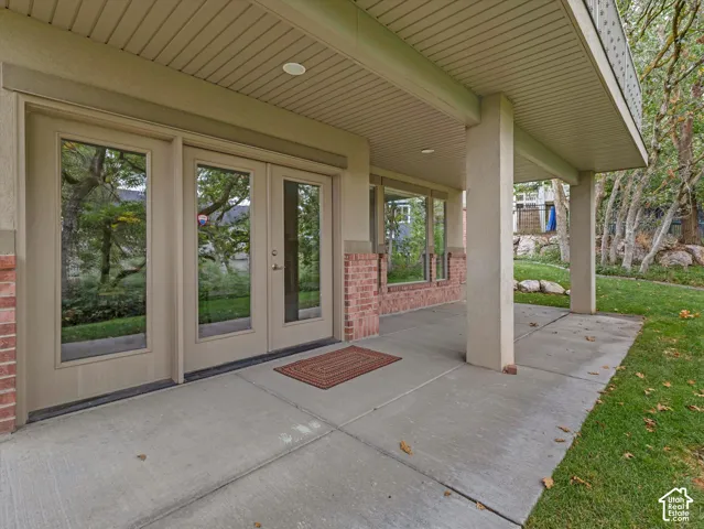 Covered concrete patio with recessed lighting, brick accents, and multiple glass-paneled doors