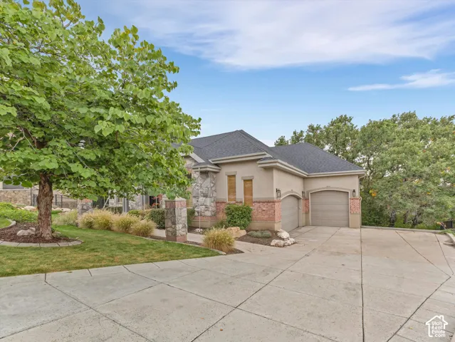 Stucco and stone exterior featuring a two-car garage, concrete driveway, and mature landscaping