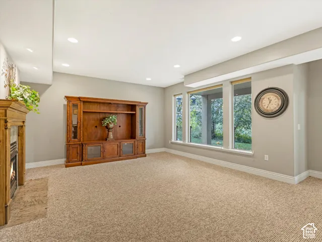 Recessed lighting illuminates the space, featuring a built-in wooden entertainment center and a fireplace with a stone surround
