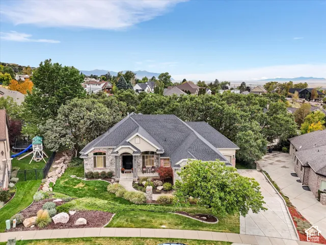 Stone and stucco facade residence with dark shingle roofing, extensive landscaping, and a multi-level driveway