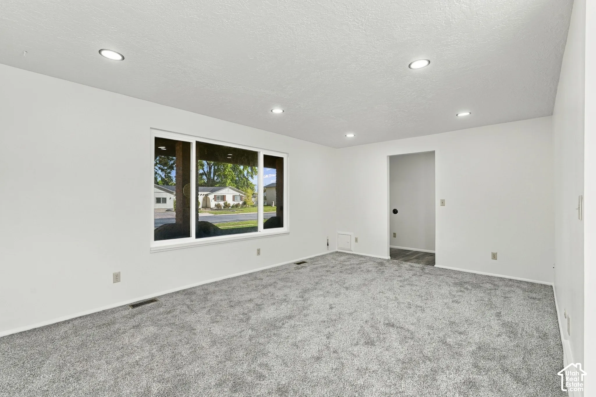 Carpet flooring, white painted walls, recessed lighting, and a large window