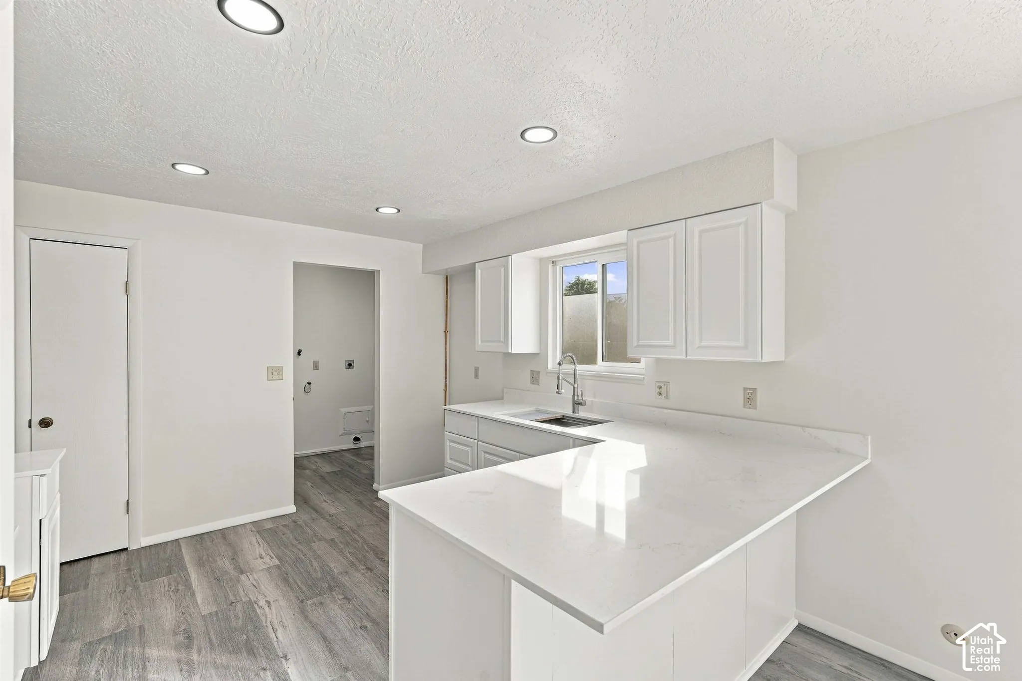White shaker cabinetry with an integrated sink, light-toned countertops, and wood-finish flooring