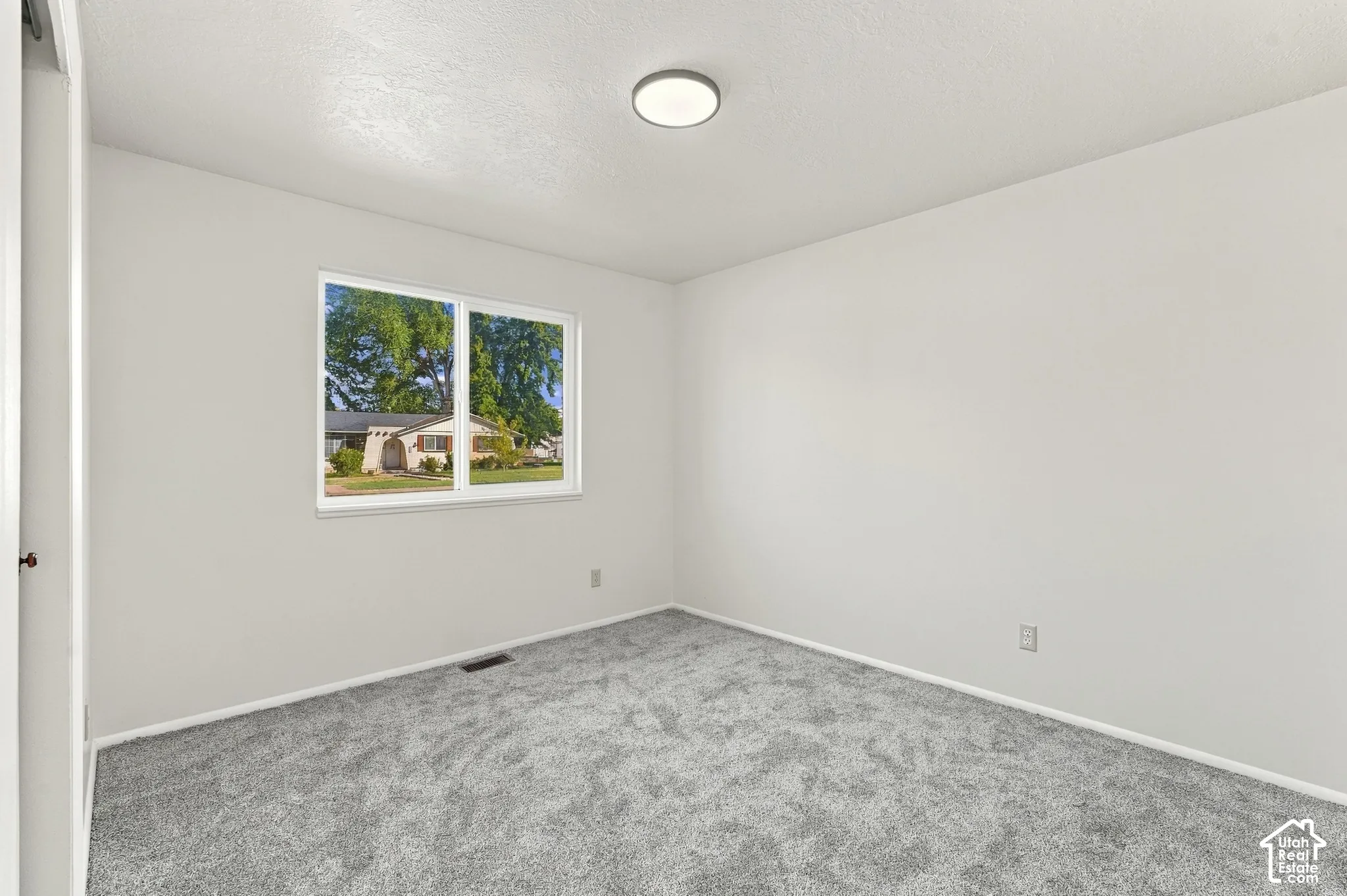 Bright interior space featuring a window, light-toned walls, gray carpeting, and an overhead flush-mount light fixture